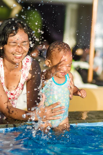 Mãe e criança brincando de respingos de água na piscina — Fotografia de Stock