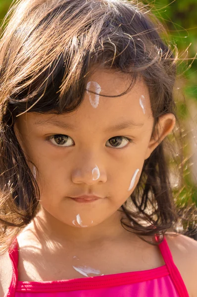 Азіатська дитина використовує сонячний лосьйон на її обличчі перед плаванням Стокове Зображення
