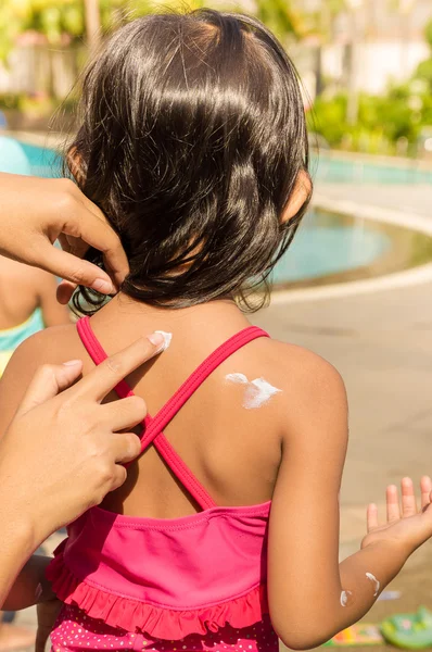 Азіатська дитина використовує сонячний лосьйон на її шкірі спини перед плаванням Ліцензійні Стокові Зображення