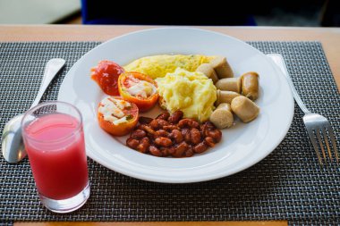 Otel sağlıklı kahvaltı menüsü patates püresi, omlet, fasulye, domates ve sosis bir bardak guava suyuyla servis edilir.