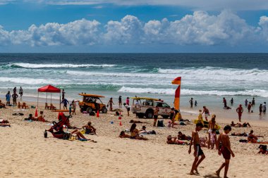 Şemsiyeli ve deniz dalgalı kalabalık bir sahil.