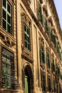 Narrow street with balconies, churches in Valletta - the capital of Malta. Southern Harbor District Sandstone buildings view with traditional closed colorful wooden balconies and church towers.