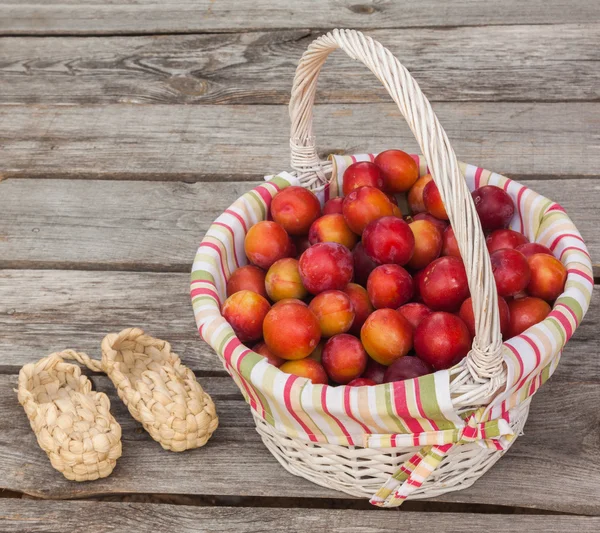 Basket filled with plums and  bast shoes — Stock Photo, Image