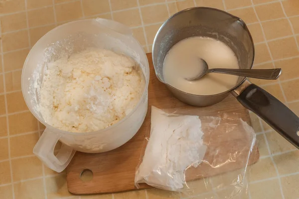 Mixer ladle with grated cottage cheese, ladle with cooked gelatin and a bag of powdered sugar for cottage cheese dessert