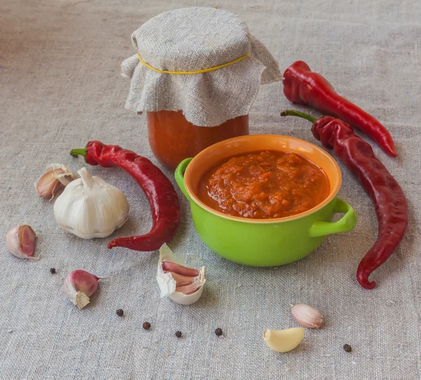 Homemade adjika next to the peppers and garlic — Stock Photo, Image