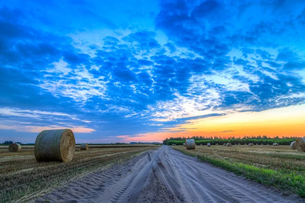 Pôr do sol sobre estrada rural e fardos de feno — Fotografia de Stock