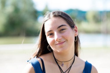 Parkta kameraya bakıp gülümseyen uzun saçlı güzel bir genç kızın yakın plan portresi.