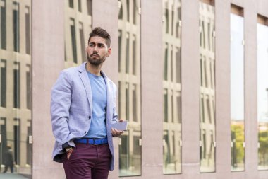 Mutlu sakallı genç adam dışarıda dikilip gözlerini kaçırırken elinde akıllı bir telefon tutuyor.