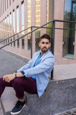 Mutlu sakallı genç adam merdivenlerde oturuyor.