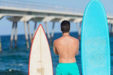Neoprene mayo giymiş yakışıklı ve çekici bir sörfçü elinde sörf tahtası, yaz sporu ve tatillerin tadını çıkardıktan sonra havalı poz veriyor.
