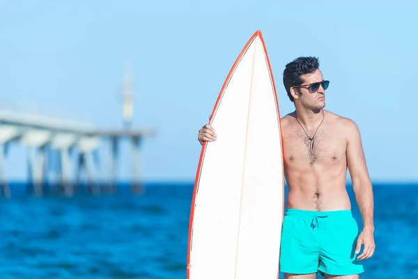 handsome and attractive surfer man in neoprene swimsuit holding surf board posing cool after surfing enjoying Summer water sport and holidays