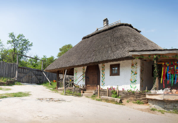 Hortica, Zaporizhia, 2015 JUNE. Zaporizhian National Sich Cossack Museum. Typical aged peasant white homestead, wooden paling and well-crane in yard. Panoramic view with space for text on blue sky