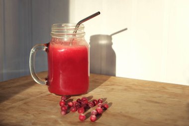 Duvardaki beyaz duvarda gölgesi olan ahşap masada taze böğürtlenli kızılcık suyu. Ev yapımı vitamin içeceği..