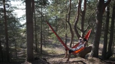 Keçeli şapkalı kişi güneşli çam ormanlarında turist hamağında tek başına dinlenir. Huzur ve sükunetin tadını çıkaran bir adam. Doğal anlar ve doğal aktiviteler..
