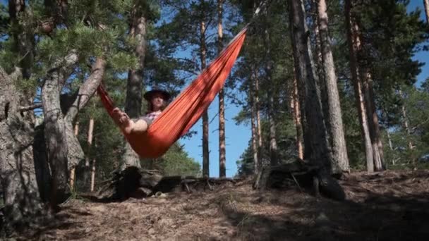 女旅行者坐在游客的吊床上 在阳光灿烂的松林里荡秋千 享受着她的孤独 和平与宁静 自然界中的自然时刻和个人活动 — 图库视频影像