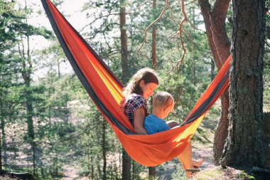 Anne ve oğul yürüyüşçüler ormandaki turist hamağında oturuyorlar. Aktif aile açık havada, çocukla seyahat ve macera