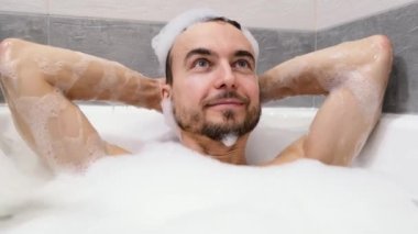 Banyoda köpükle rahatlayan yakışıklı sakallı adamın portresi. Ev banyosunda spa tedavisi. İnsan sağlığı, vücut bakımı ve kendini sevme kavramı..