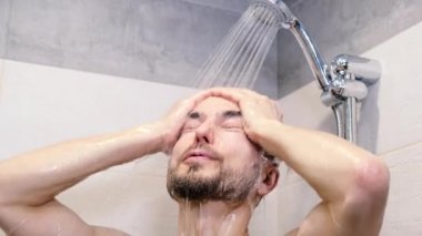 Erkek sağlığı, vücut bakımı ve kişisel hijyen konsepti. Yakışıklı sakallı adam banyoda duş alıyor, gülümsüyor ve suyun altında duş almaktan zevk alıyor. Sabah rutini.