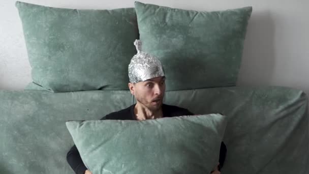 Verschwörungstheoretiker Mann Mit Zinnfolienhut Versteckt Sich Hinter Kopfkissen Während Hause — Stockvideo