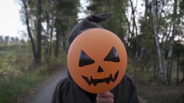 身着僧人或巫师服装的神秘男子 在秋天的路上独自站着 手里拿着橙色的气球 脸上挂着令人恐怖的南瓜头像 万圣节的概念 — 图库视频影像