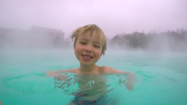 地熱スパ リゾート 山の中の屋外の温泉プールで楽しんでいるかわいい子供の男の子 お湯で入浴 オフシーズンの旅行の魅力 — ストック動画