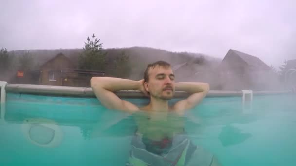 地熱スパ リゾート 山の中の屋外の温泉プールでリラックスしてハンサムな男 お湯で入浴 オフシーズンの旅行の魅力 ウェルネスとセルフケアの概念 — ストック動画