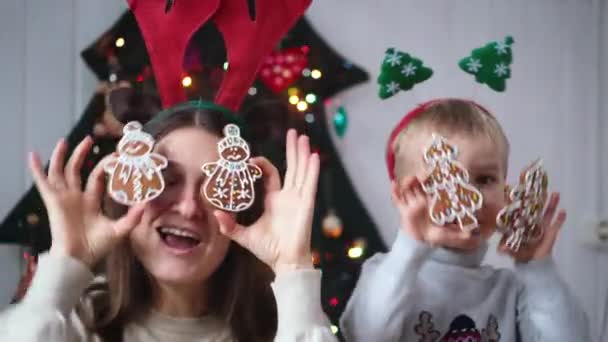 陽気な母親と彼女の小さな子供男の子持っています楽しい近くに代替クリスマスツリーを保持ジンジャーブレッドクッキー近く目 — ストック動画