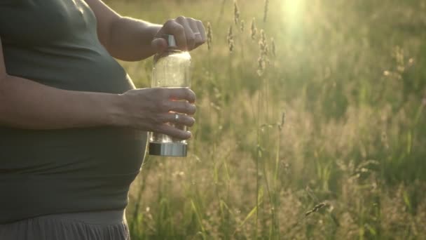 Беременная Женщина Пьет Воду Многоразовой Стеклянной Бутылки Открытом Воздухе Закате — стоковое видео
