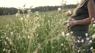 Hamile kadın karnına dokunuyor, yaz gününün tadını çıkarıyor. Çiçek açan alanda hamile bir kız var. Annelik, bebek beklentisi konsepti.