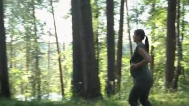 Aktif hamile milenyum kadını yaz parkında koşuyor. Müstakbel anne sağlıklı yaşam tarzı egzersizi yapıyor dışarıda koşuyor. Hamilelik sporu ve spor eğitimi konsepti.