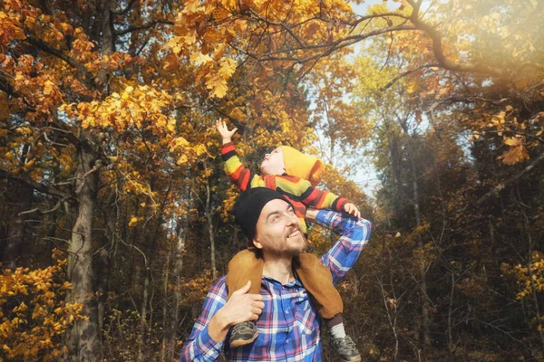 森の黄金の秋の木を背景に父の肩に座ってかわいい子供の男の子 秋の季節に父と息子の屋外で一緒に時間 — ストック写真