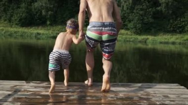 Babası ve küçük oğlu yaz güneşli bir günde tahta iskeleden göle atlıyorlar. Aile tatili, tatil.