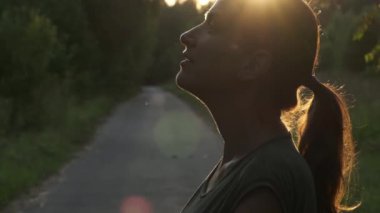 Orta yaşlı, beyaz bir kadının günbatımında doğanın tadını çıkarırken çekilmiş bir portresi. Yavaş çekim.