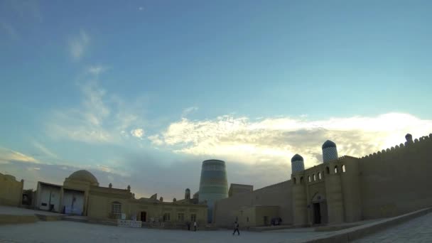 KHIVA, UZBEKISTAN - OCTOBER 1, 2015: Tourists and locals walking under the walls of the Kuhna Ark citadel and Kalta Minor Minaret at sunset on October 1 in Khiva, Uzbekistan, Central Asia. Time-lapse. — Stock Video