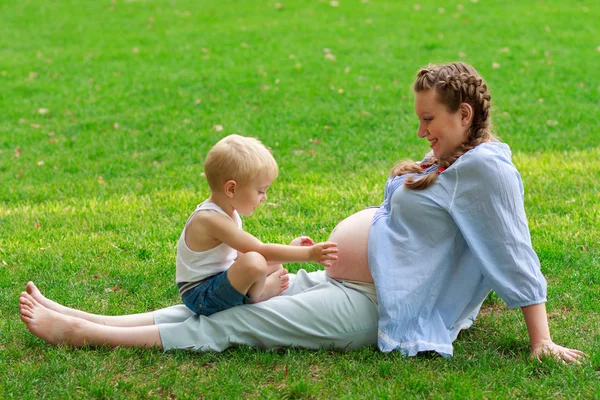 Pregnant woman and her son on the green grass — Stock Photo, Image