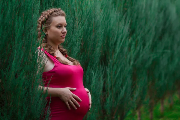Pregnant woman in red dress among green bushes, horizontal — Stock Photo, Image