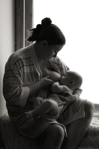 Donna che allatta vicino a una finestra, pisolino per bambini, bianco e nero Foto Stock