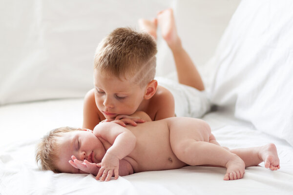 Маленький мальчик смотрит на свою новорожденную сестру в помещении
