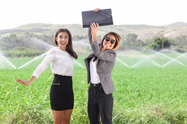 Two business women with a laptop in a field, jumping and celebrating success