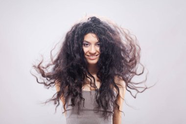 Havada uzun kıvırcık saçlı güzel esmer kız, stüdyo portresi. Mutlu gülen yüz ifadesi.
