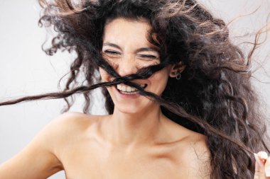 Havada uzun kıvırcık saçlı güzel esmer kız, stüdyo portresi. Komik sakar surat ifadesi..