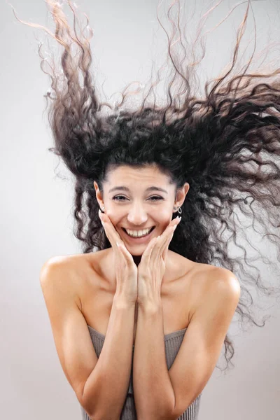 空気中の長い巻き毛の美しいブルネットの女の子 スタジオの肖像画 笑顔の表情 — ストック写真
