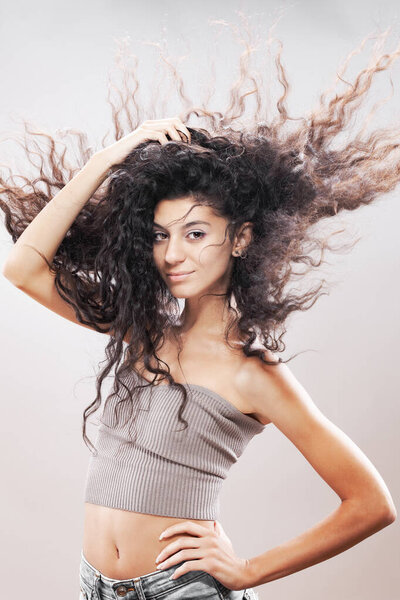 Красивая брюнетка с длинными вьющимися волосами в воздухе, студийный портрет. Серьезное выражение лица.