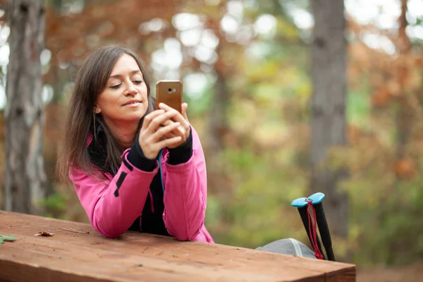 远足的女孩躺在森林的长椅上休息 带粉色夹克衫的背包客手持手机 — 图库照片