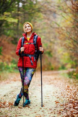 Sırt çantası ve sırıkla bir patikada duran yürüyüş yapan kız. Kameraya bakıyorum. Gezi ve sağlıklı yaşam tarzı sonbahar mevsiminde açık havada
