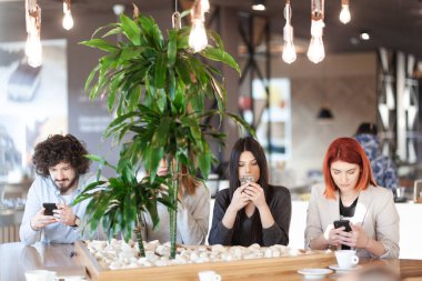 Bir kafede oturup telefonlara bakan dört arkadaş..