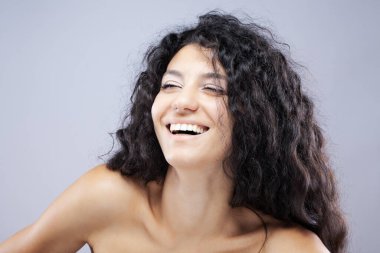 Uzun kıvırcık saçlı, stüdyo portresi olan güzel esmer kız. Gülen yüz ifadesi.
