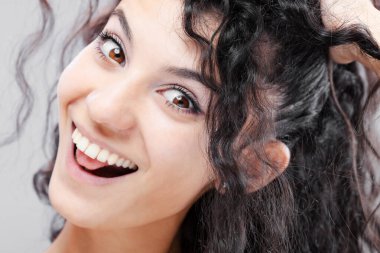 Uzun kıvırcık saçlı, stüdyo portresi olan güzel esmer kız. Komik sakar surat ifadesi..