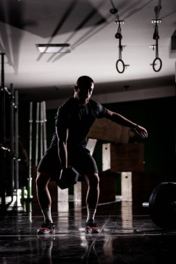 Çok ağır ağırlık kaldıran kaslı bir atletin silüeti. Adam içeride çalışıyor.