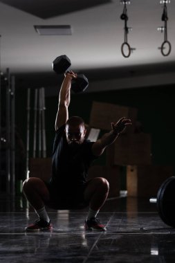 Çok ağır ağırlık kaldıran kaslı bir atletin silüeti. Adam içeride çalışıyor.